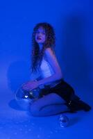 Sensuality woman holding disco ball, looking at camera. Woman kneeling in blue neon colored lighting photo