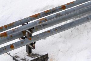 External city central heating pipes protruding from snow. Pipes in rusty thermal insulation jackets photo