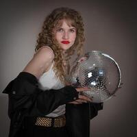 Young adult pin up girl from Gen Z with long curly hair holds mirror disco ball, looking at camera photo