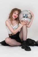 Cheerful young adult pin up girl holding and presses mirror disco ball to herself, looking at camera photo