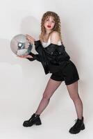 Confident young adult pin up girl holding disco mirror ball and looking at camera, standing on white photo