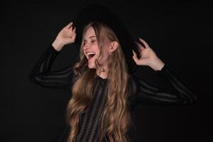 Woman with closed eyes and toothy smile, turning head to side and holding brim of felt hat photo