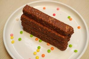 Chocolate bars on a white plate with colorful candies in the background photo