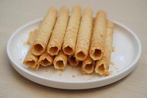 Pile of Cigarette Russe rolled biscuits on white plate on wooden table. photo