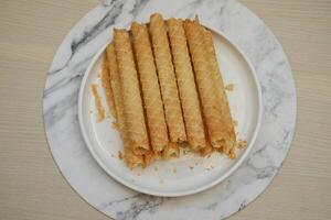 Pile of Cigarette Russe rolled biscuits on white plate on wooden table. photo