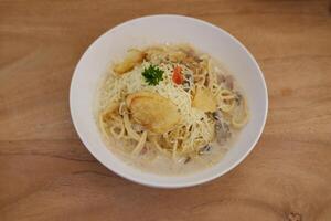 Spaghetti with mushroom sauce and cheese in white bowl on wooden table photo