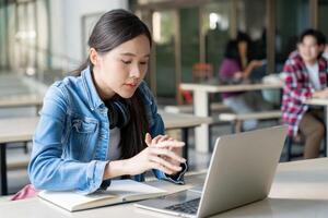 asiático mujer hembra estudiante emocionado comprobación idioma prueba resultados en ordenador portátil. sonrisa niña contento estudiar en línea. libro en Universidad instalaciones. retrato hembra en internacional Asia universidad. educación foto