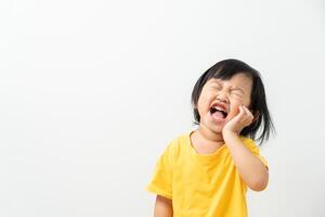 pequeño asiático niña prensas mano a mejilla, sufre desde dolor en diente. dientes decadencia, dental problemas, niño emociones y facial expresión, oral salud cuidado, reduciendo dulces, flúor revestimiento foto