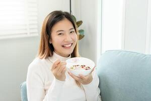 sano alimento. hermosa hembra niña disfrutar comer yogur, Granola, Fresco frutas en desayuno salud en casa. contento joven mujer sonrisa en Mañana bueno emoción. haciendo dieta, desintoxicación, dieta, limpiar comer, vegetariano foto