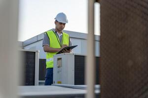 asiático mantenimiento ingeniero trabajos en el techo de fábrica. contratista inspeccionar compresor sistema y planes instalación de aire condición sistemas en construcción. Lista de Verificación, inspector, controlar foto