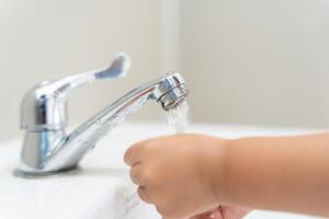 pequeño niño manos lavar con jabón burbujas y enjuague con limpiar agua a evitar y detener el untado de gérmenes después espalda a hogar, virus o COVID-19. bueno salud y bueno personal higiene, virus, bacterias foto