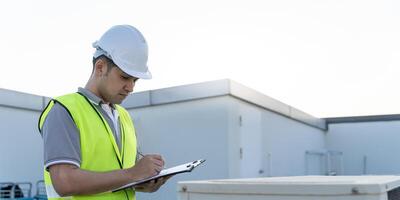 Asian maintenance engineer works on the roof of factory. contractor inspect compressor system and plans installation of air condition systems in construction. Checklist, inspector, control photo