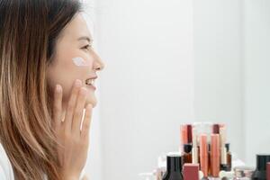 hermosa asiático mujer sonrisa utilizar crema para bueno piel. cara de un sano mujer aplicar crema y constituir. anuncio para piel crema, anti arrugas, bebé rostro, blanqueo, hidratante, apretar poros suero foto