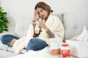 Young Asian woman having high fever while checking body temperature, female sneezing and runny nose with seasonal influenza, allergic, digital thermometer, virus, coronavirus, illness, respiratory photo