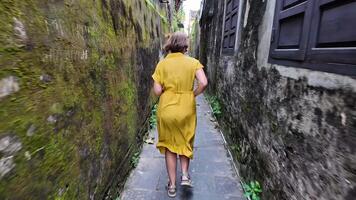 A person in a yellow dress briskly walking through a narrow, mossy alleyway, capturing the essence of urban exploration and adventure travel video