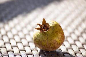 An unripe green pomegranate on a wicker brown table in the sunlight. An autumn fruit. Healthy food. Horizontal photo