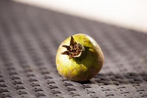 An unripe green pomegranate on a wicker brown table in the sunlight. An autumn fruit. Healthy food. Horizontal photo