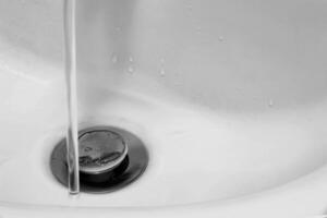 Detail of ceramic white sink in modern bathroom with chrome drain and tap water. Horizontal. For text. photo