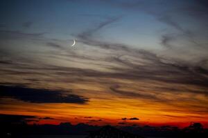 Red-orange sky at sunset in twilight evening with dark clouds and moon. Nature sky. Background, horizon golden sky, sunrise cloud magnificent, twilight sky. photo