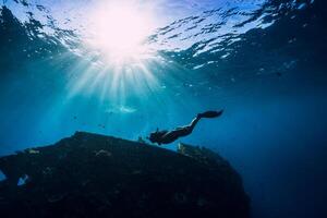 Free diver girl in pink swimwear with fins swimming underwater at wreck ship. Freediving in the ocean photo