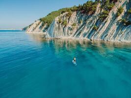 Man on stand up paddle board in blue sea. Surfer walking on SUP board in sea with incredible landscape. Aerial view photo