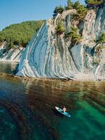 Man relax on stand up paddle board in sea. Surfer walking on SUP board in summer sea with incredible landscape. Aerial view photo