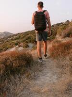 Hiker man with backpack walk on sea coastline with warm sun light. photo