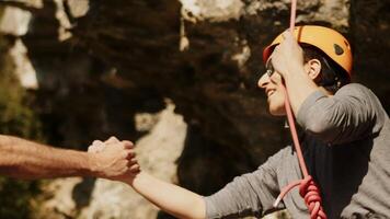 Close-up of a Male Climber in Gray and Orange Gear Shaking Hands with a Fellow Climber Against a Rocky Cliff Background, Symbolizing Teamwork and Achievement in Extreme Sports video