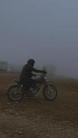 solitario motociclista montando mediante un brumoso paisaje en un Clásico motocicleta, capturado en un vertical marco destacando el estado animico de soledad y aventuras video