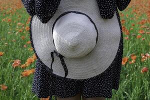 Close-up of female hands holding summer hat the background of field with poppies. Vacation concept photo