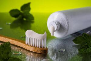 Close up tube of toothpaste and bamboo toothbrush on wet reflective surface with fresh mint leaves. Oral care featuring.Concept oral health and care. International Dentist Day. National Brush Day photo