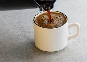 Pouring hot coffee from a coffee pot into a cup on the table photo