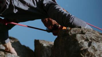 Rock climber woman climbing up a sheer cliff in mountain gear. A rock climber in a helmet and with climbing ropes is doing rock climbing. The power of women. A cinematic shot. The idea of success and video