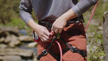 female athletic Rock climber preparing to climb rocks. woman climber checking rope knot on harness under cliff getting ready to climb video