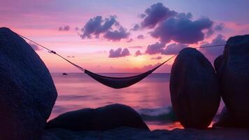 A hammock hangs between two large boulders on a remote island overlooking a vast expanse of ocean. As the sky turns shades of pink and purple you close your eyes and video