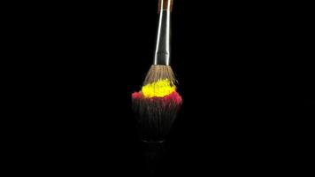 Makeup brushes touch each other on black dark background and small particles of color cosmetics, super slow motion, 1000 fps FullHd video