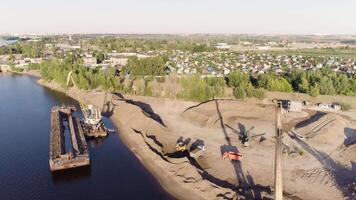 Construction cranes and trucks on shore. Scene. Top view of clearing of construction site on lake shore. Start of construction on lake shore on sunny day video