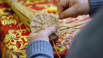 manos Costura el fondo de un Paja cesta. Arte. un hombre tejidos un redondo parte de Paja y leña menuda con su manos. artesanía son aprendió a el ruso festival video