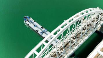 Top view of boat passing under bridge. Action. Long cargo boat sails under bridge with highway. Boat under bridge with turquoise water video