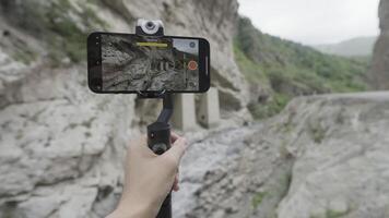 Shooting mountains and waterfalls. Action. The phone stands on a stand and shoots beautiful landscapes with mountains and a small dripping waterfall . video