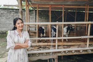 Smiling young Asian woman standing in front of traditional cage made from wood and bamboo in Indonesia rural area with goat inside photo