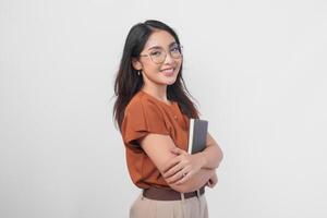 confidente sonriente asiático mujer vistiendo marrón camisa y los anteojos participación documento libro mientras mirando a el cámara aislado terminado blanco antecedentes. foto