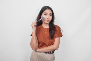 joven asiático mujer participación maquillaje cepillo a aplicar sonrojo mientras consiguiendo Listo con puchero labios expresión aislado blanco antecedentes. foto