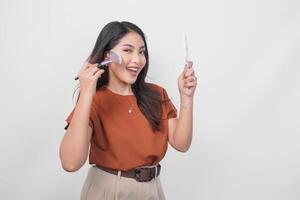 Beautiful young female holding mirror and makeup brush to apply blush using new cosmetics while getting ready isolated white background. photo