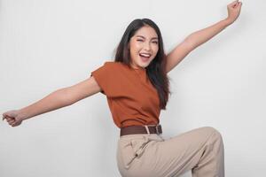 Cheerful Asian woman in brown shirt dancing with excited expression and having fun gesture over isolated white background. photo