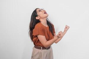 A young Asian woman wearing brown shirt and eyeglasses with a happy successful expression isolated by white background. photo