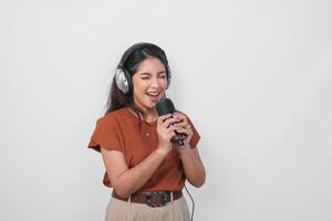 Overjoyed young woman wearing brown shirt and headphone to listen music and singing along isolated over white background. photo