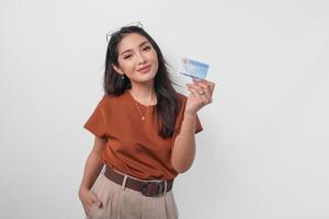 Confident young Asian woman wearing brown shirt is showing identity card Indonesia to the camera over white background. photo