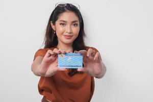 Confident young Asian woman wearing brown shirt is showing identity card Indonesia to the camera over white background. photo