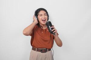 Overjoyed young woman wearing brown shirt and headphone to listen music and singing along isolated over white background. photo